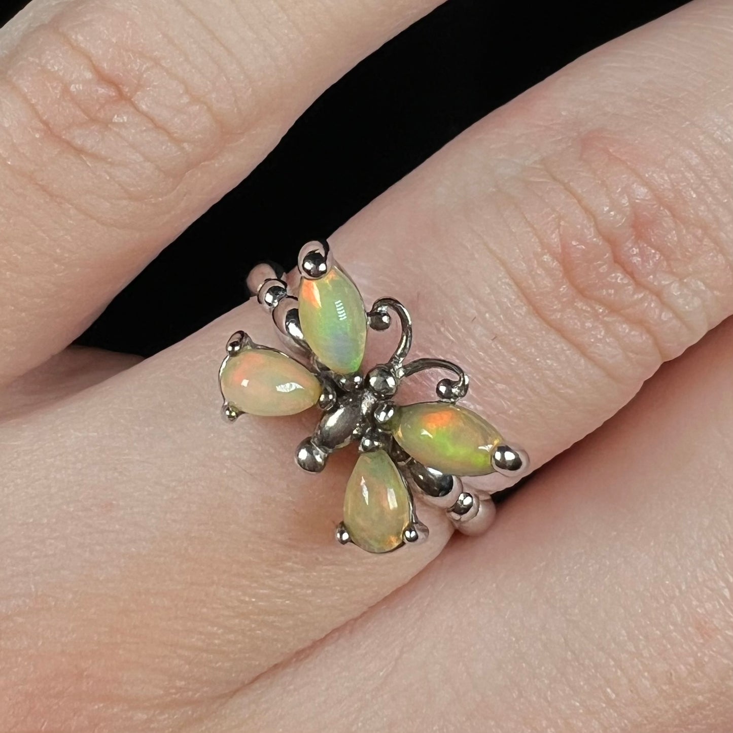Close-up front view of a sterling silver Ethiopian opal butterfly ring, worn on a finger against a black background.