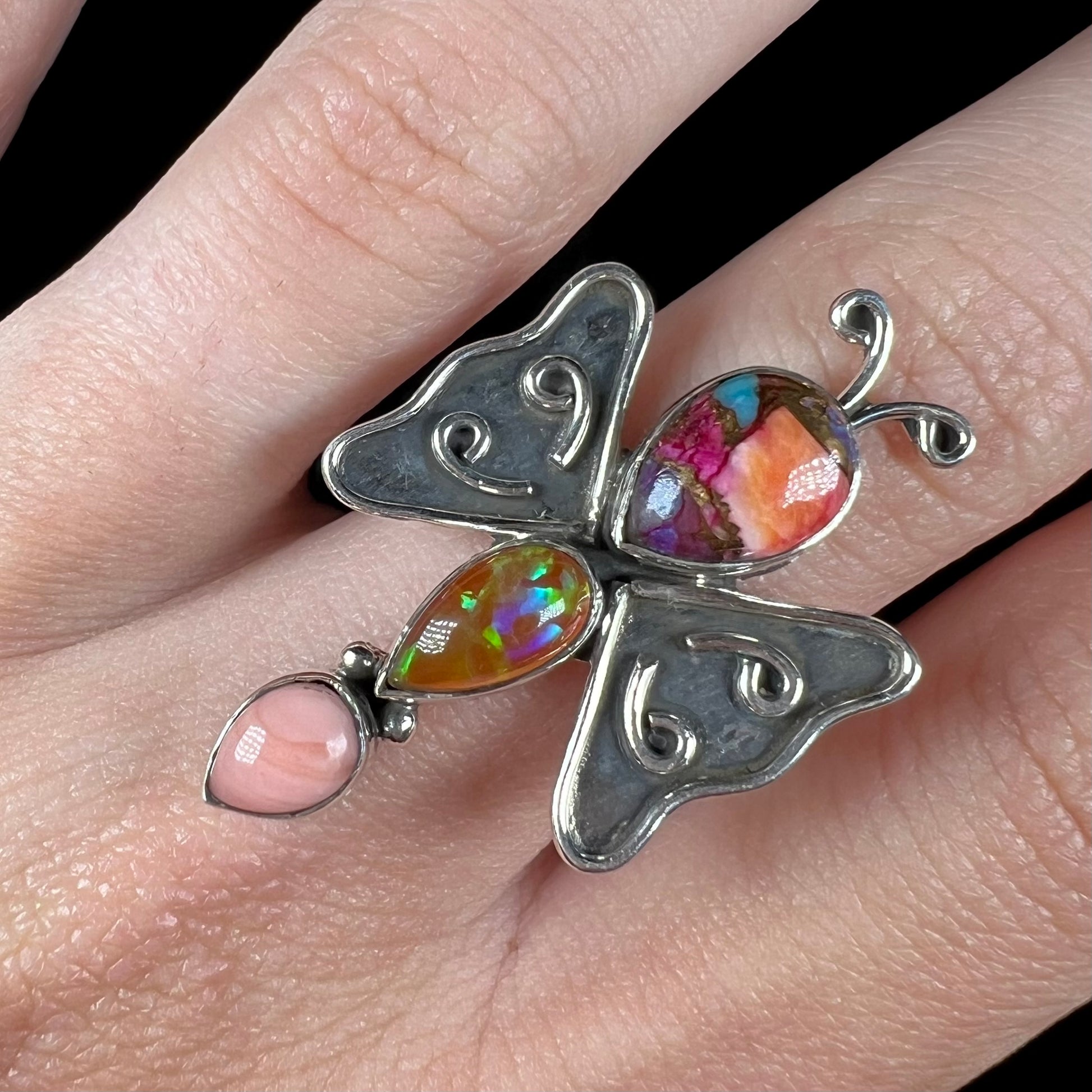 Close-up of a handmade opal butterfly ring made from sterling silver, worn on a finger and shown from the front.