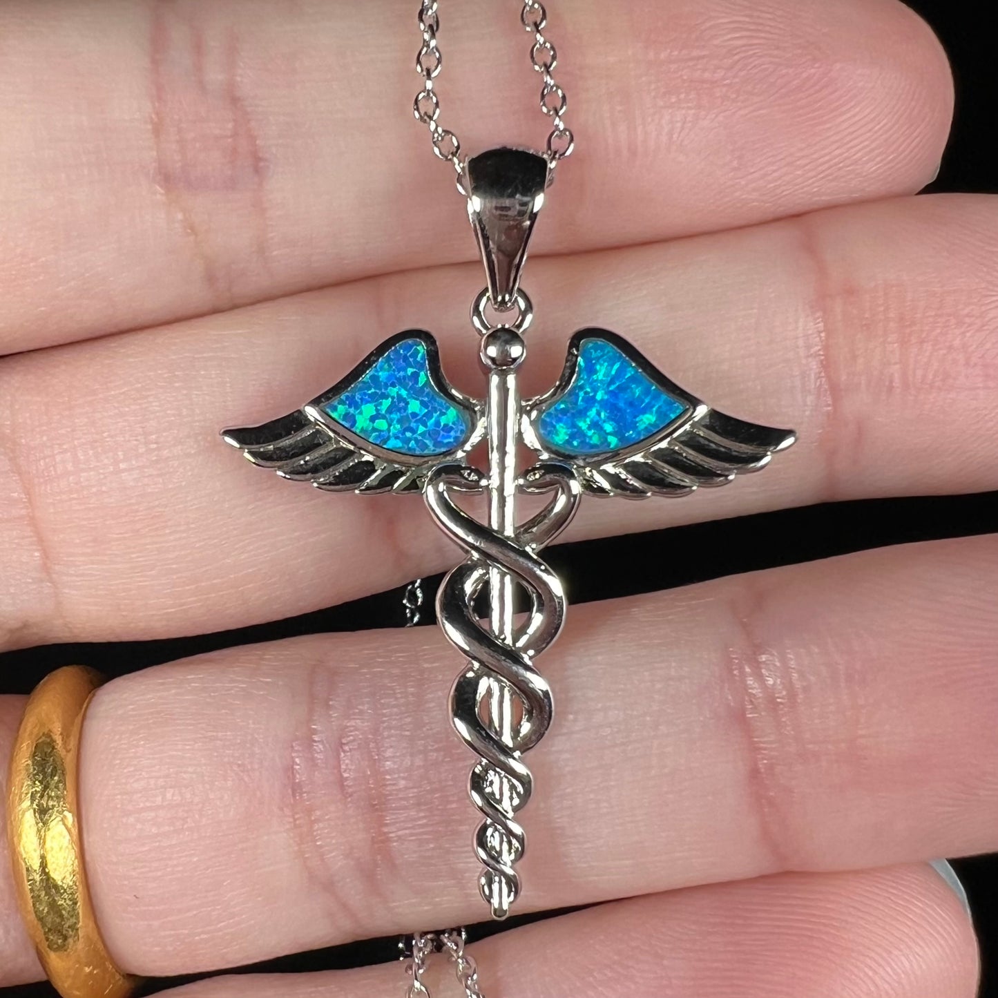 A silver plated medical caduceus pendant with blue lab-created opal inlay.