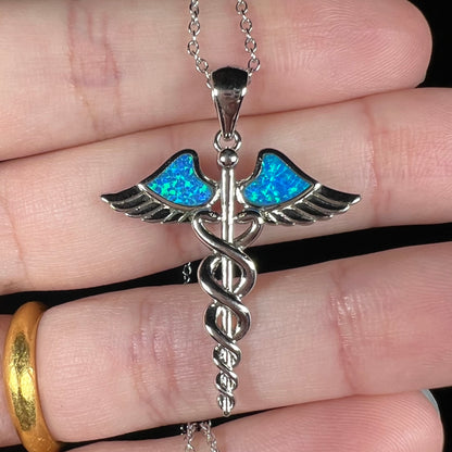 A silver plated medical caduceus pendant with blue lab-created opal inlay.