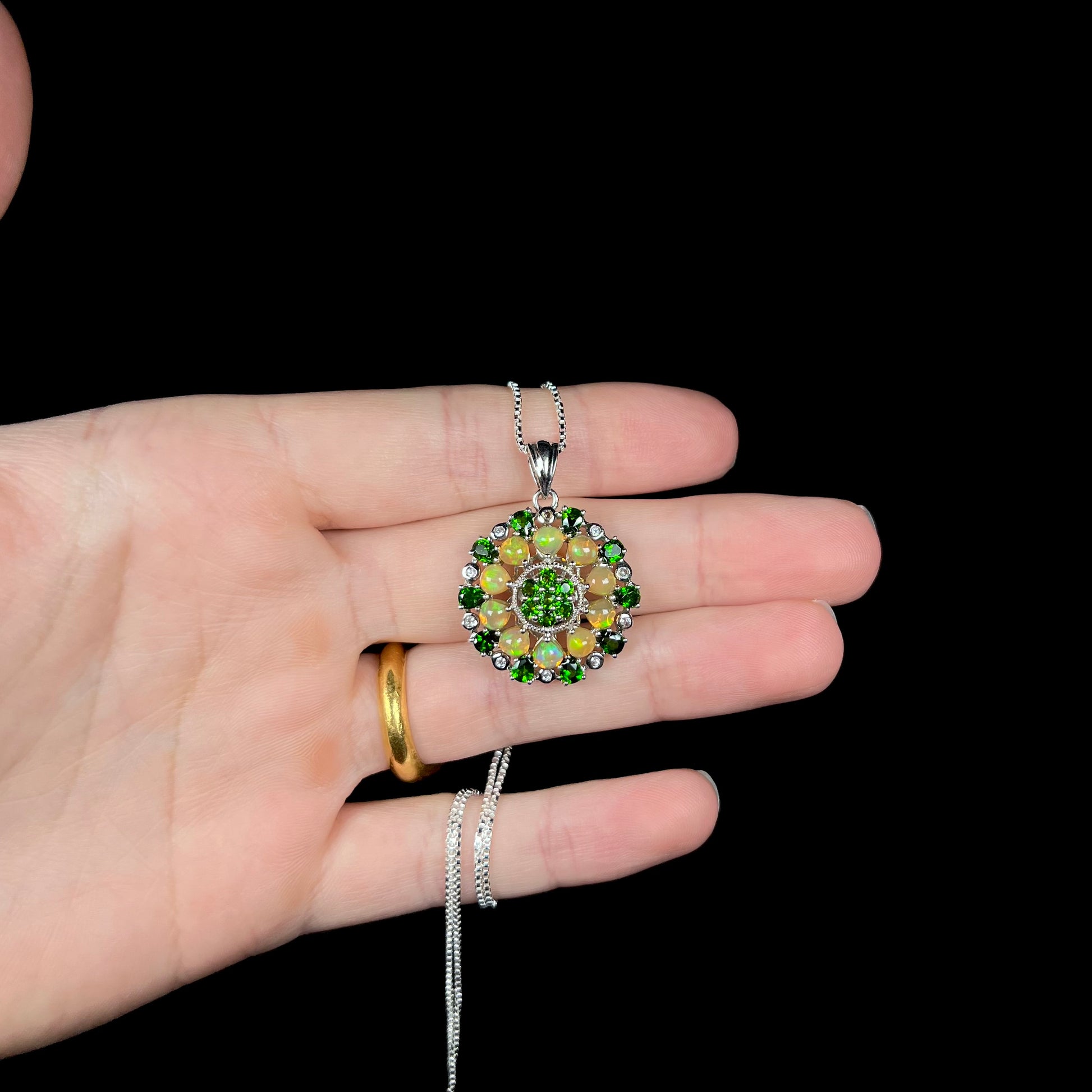 A silver opal and chrome diopside necklace, held in a hand against a black background.