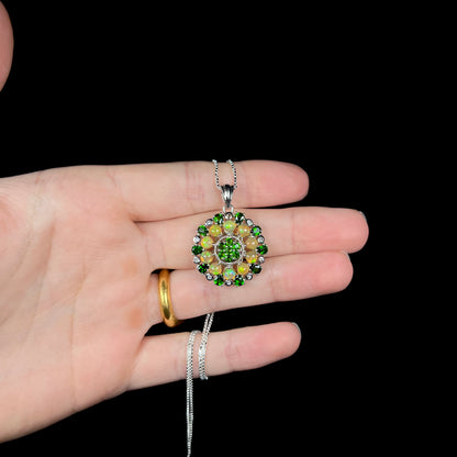 A silver opal and chrome diopside necklace, held in a hand against a black background.