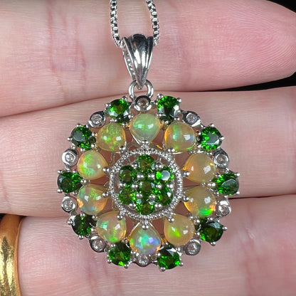 Close-up front view of a fire opal and chrome diopside pendant, held in a hand.
