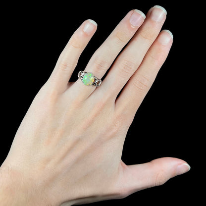 A platinum opal crisscross ring worn on a hand.  The opal is half green, half orange.