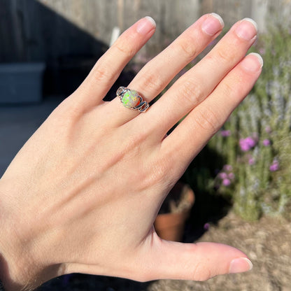 A 2.20ct opal crisscross ring cast in platinum worn on a hand in the sunlight.