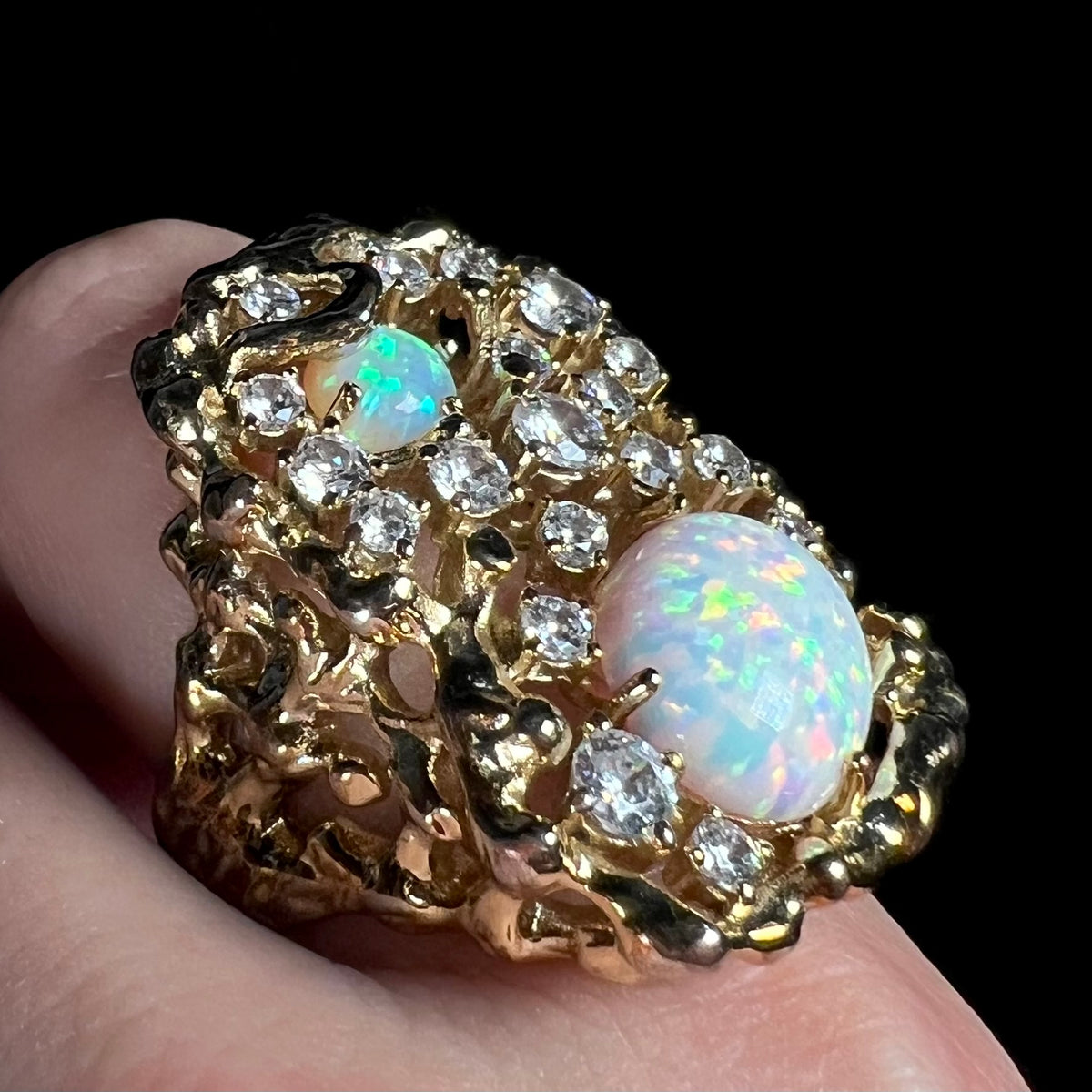 An opal and cubic zirconia ring with a large, 1970s-inspired brutalist design shown close-up from angle on finger.