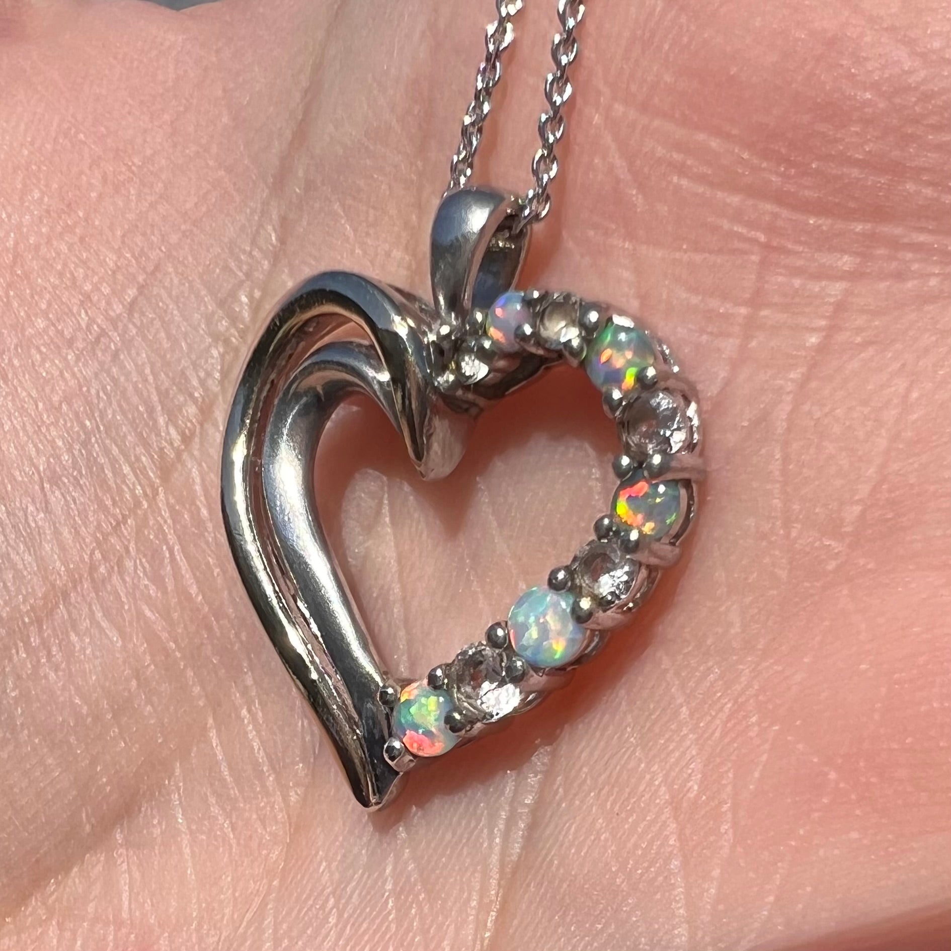 A two-tone sterling silver and yellow gold lab-created opal and CZ heart necklace shown in sunlight at an angle.