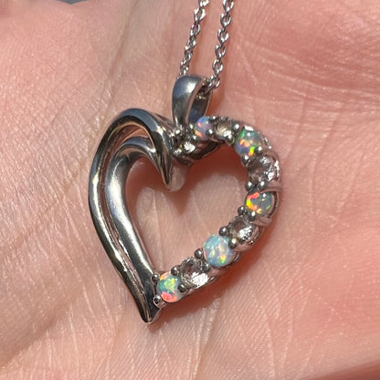 A two-tone sterling silver and yellow gold lab-created opal and CZ heart necklace shown in sunlight at an angle.