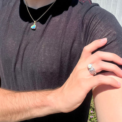 A round Australian white opal and CZ ring in white base metal worn on a hand that's resting on the model's opposing shoulder.