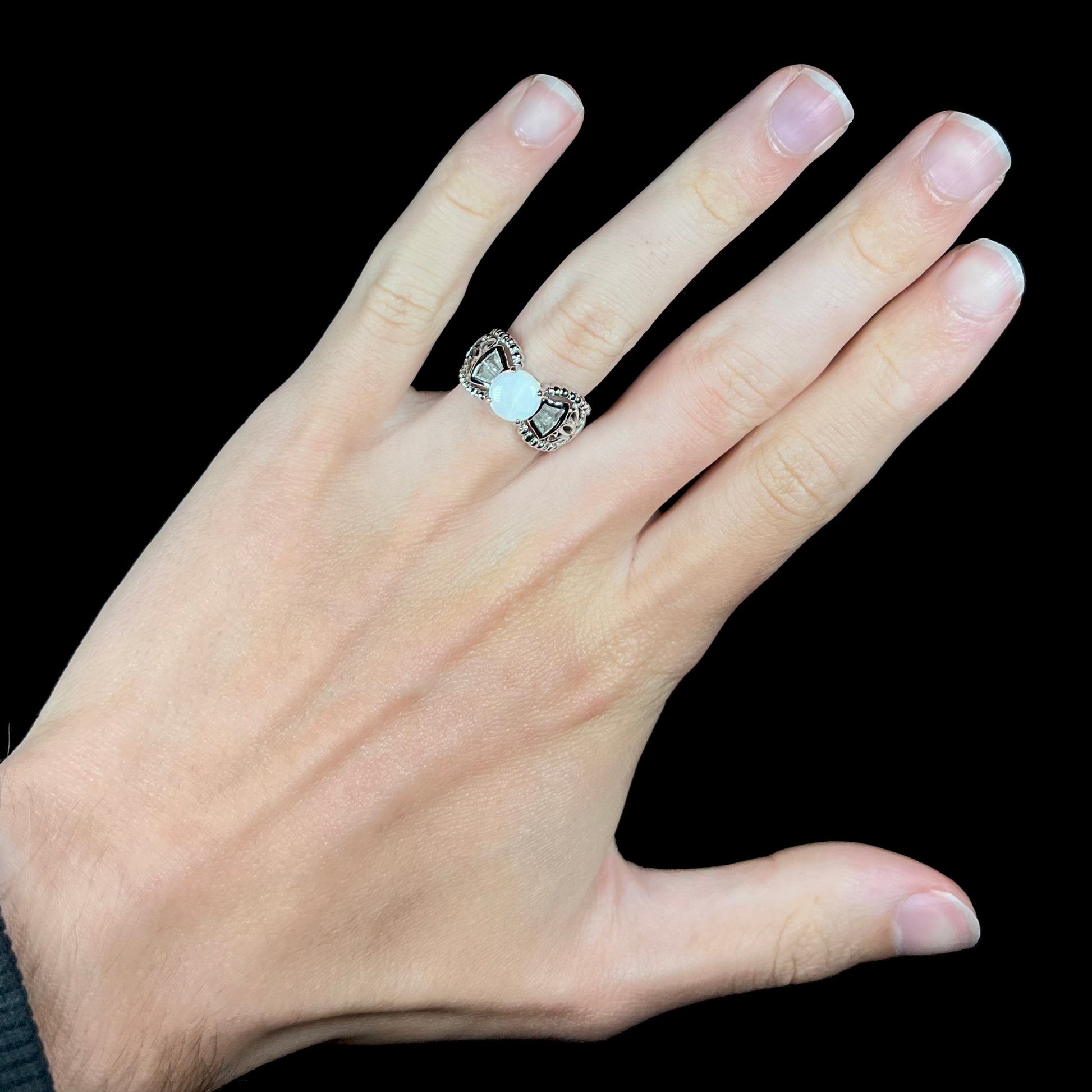 A round Australian white opal and CZ ring in white base metal worn on a hand against black background.