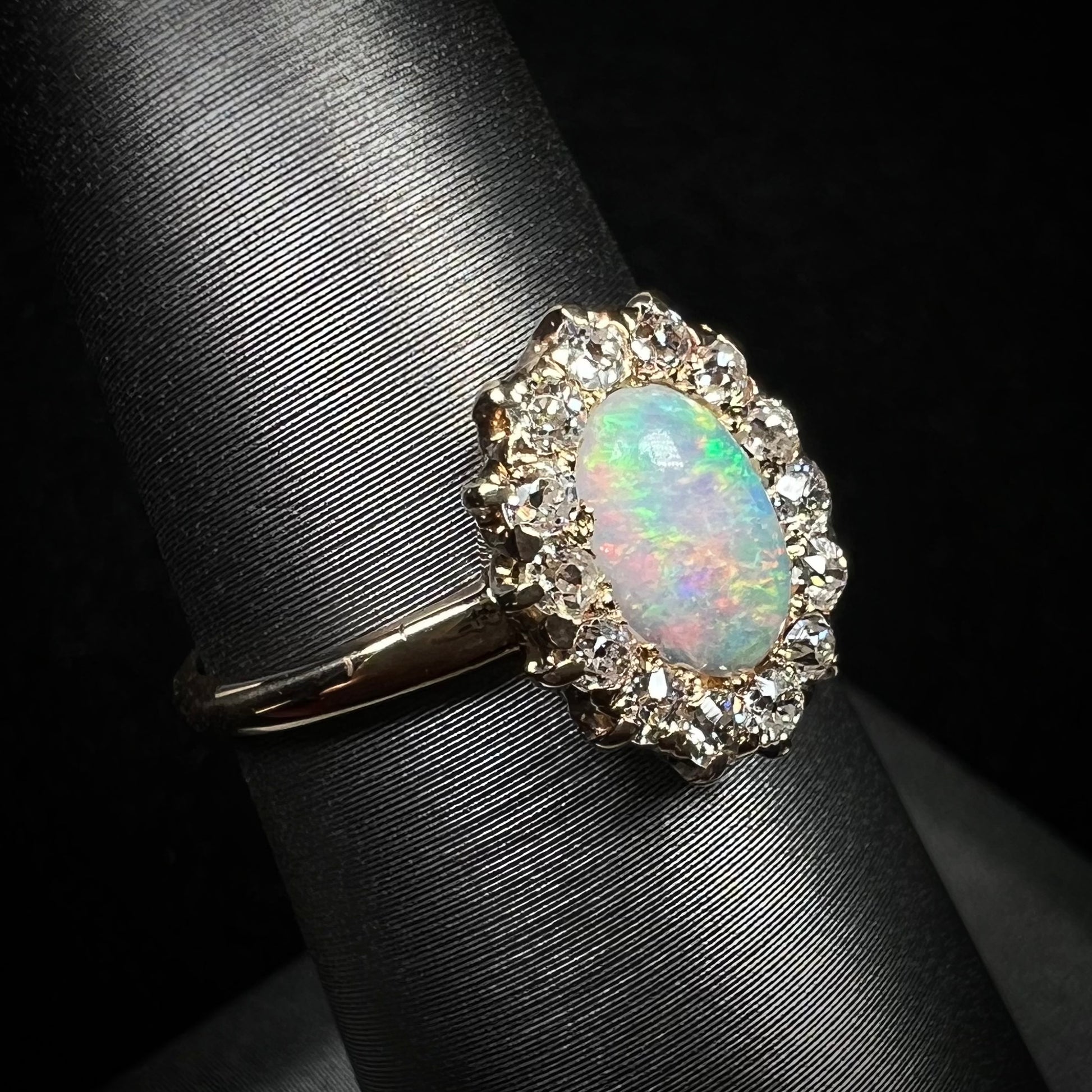 The diagonal angle of an antique, Edwardian era opal and diamond halo ring.  The opal shines green and purple colors.