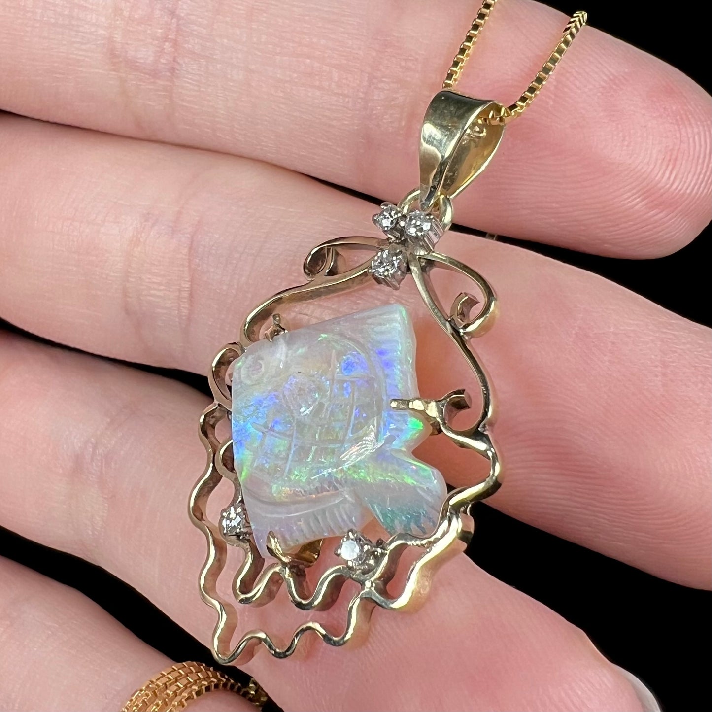 Carved Australian opal fish and diamond-accented pendant in 14k gold, shown close-up from angle in hand