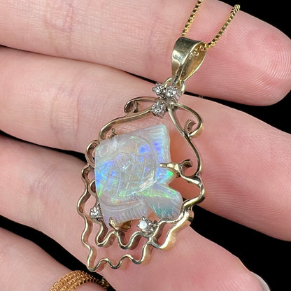 Carved Australian opal fish and diamond-accented pendant in 14k gold, shown close-up from angle in hand