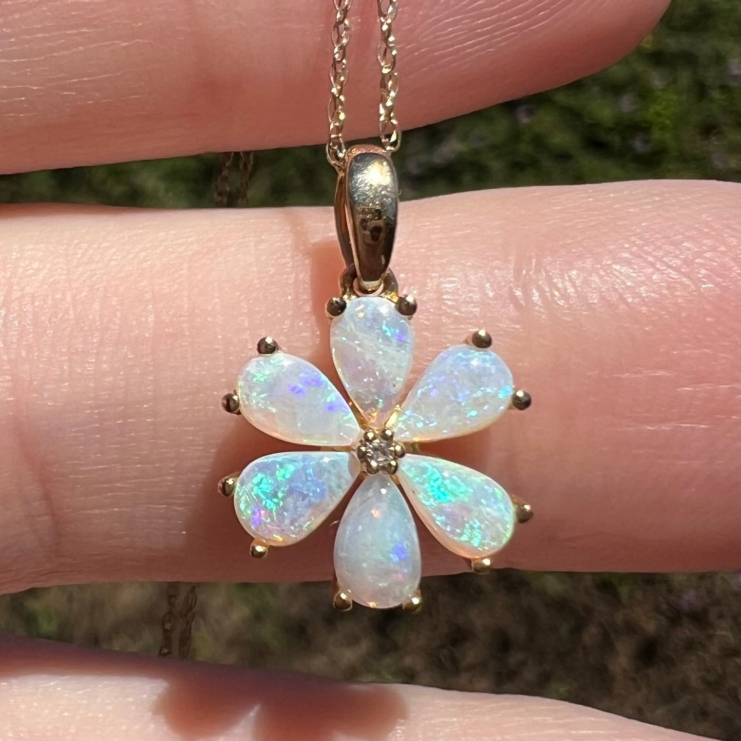 Close-up of Australian opal and diamond flower pendant held resting on finger in sunlight