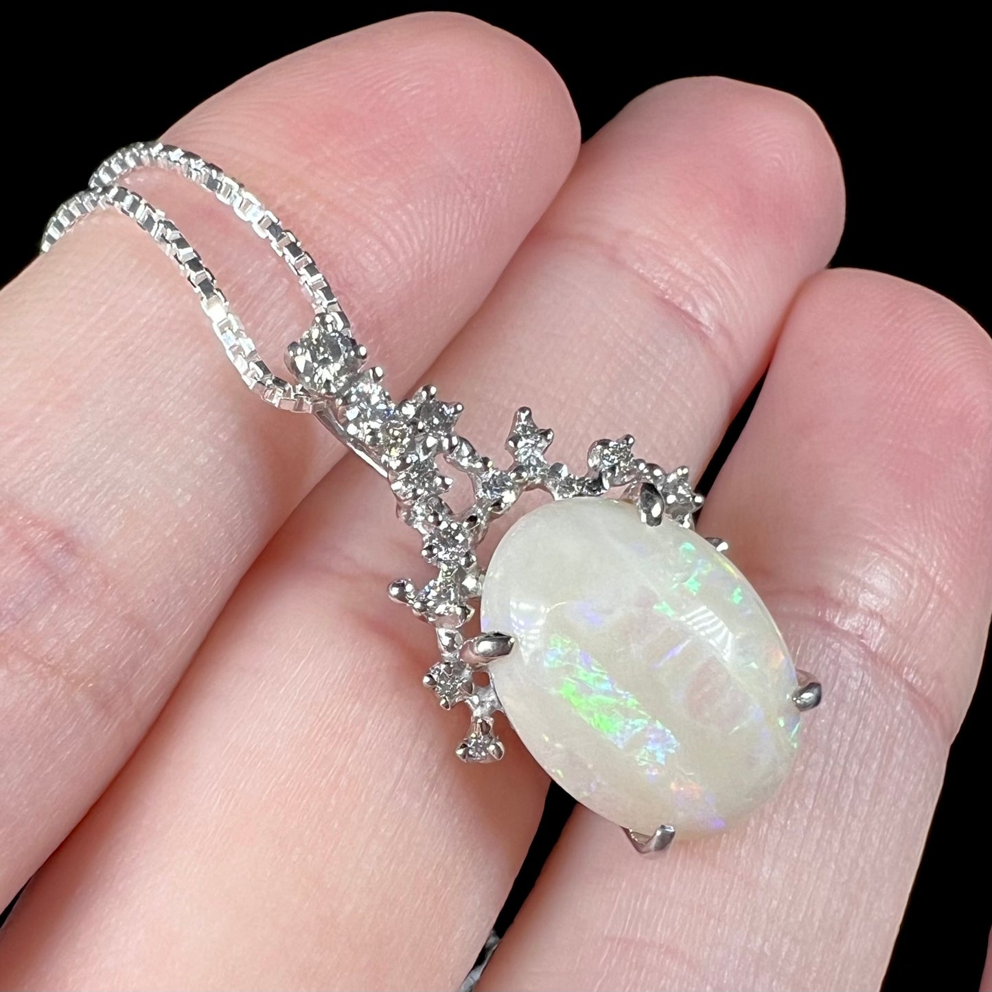 An angled macro close-up of an opal and diamond necklace, with a subtle green stripe visible.