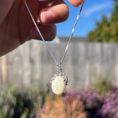 An opal and diamond necklace being dangled outdoors in natural light, where the green flash appears more vibrant.