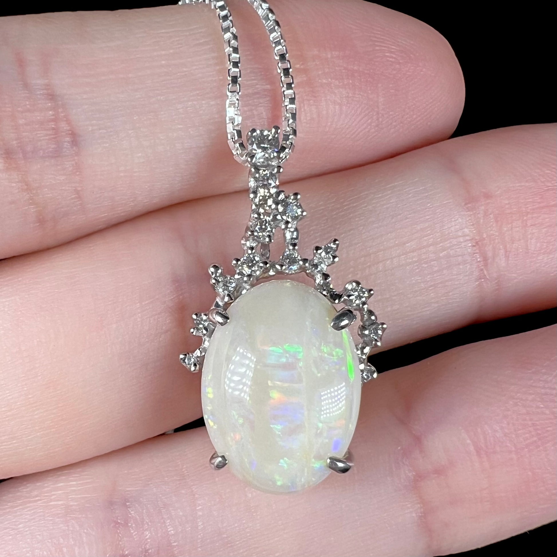 A macro close-up of an opal and diamond necklace on fingers, showing intricate details of the pendant.