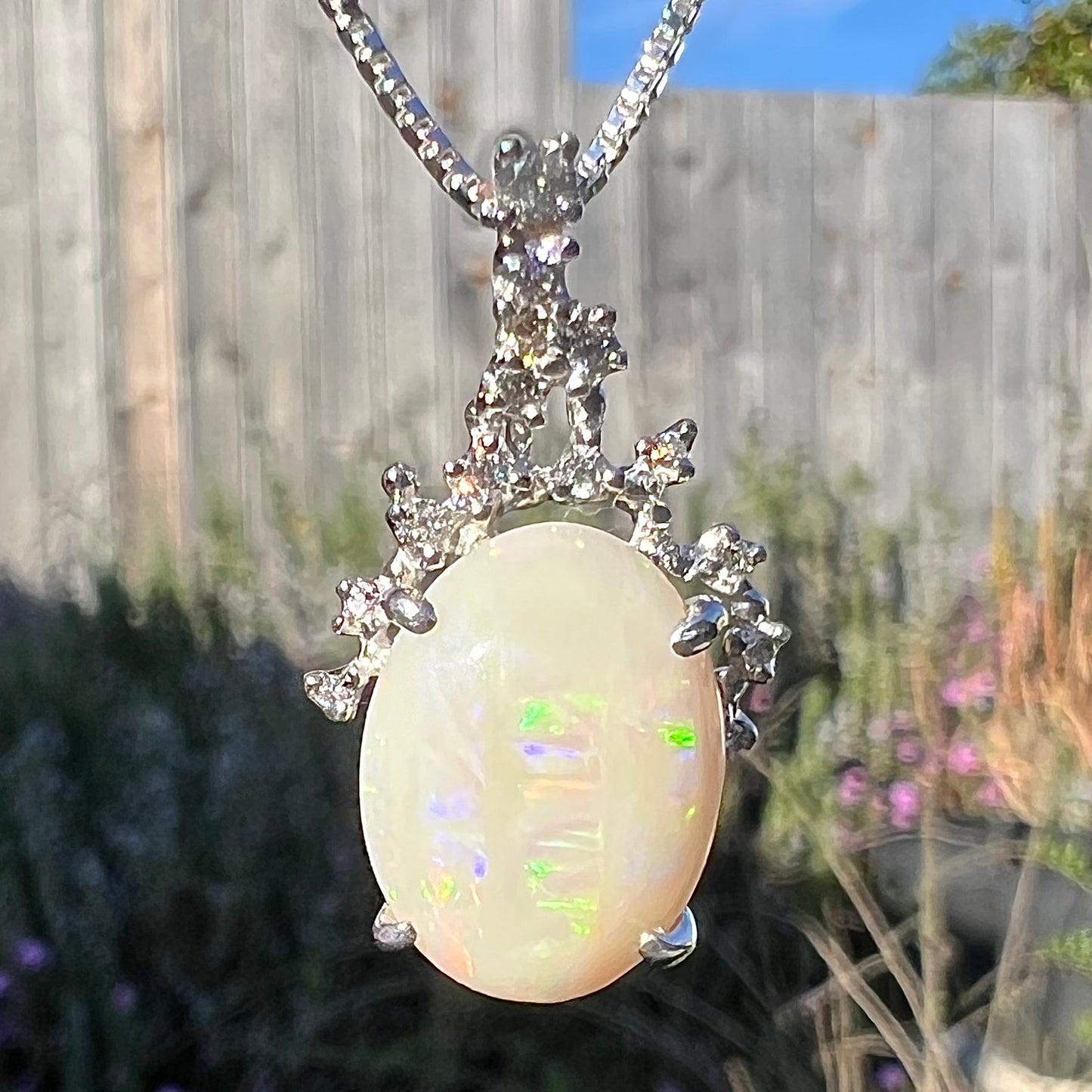 A macro close-up of an opal and diamond necklace in natural sunlight, showing subtle green and purple flashes.