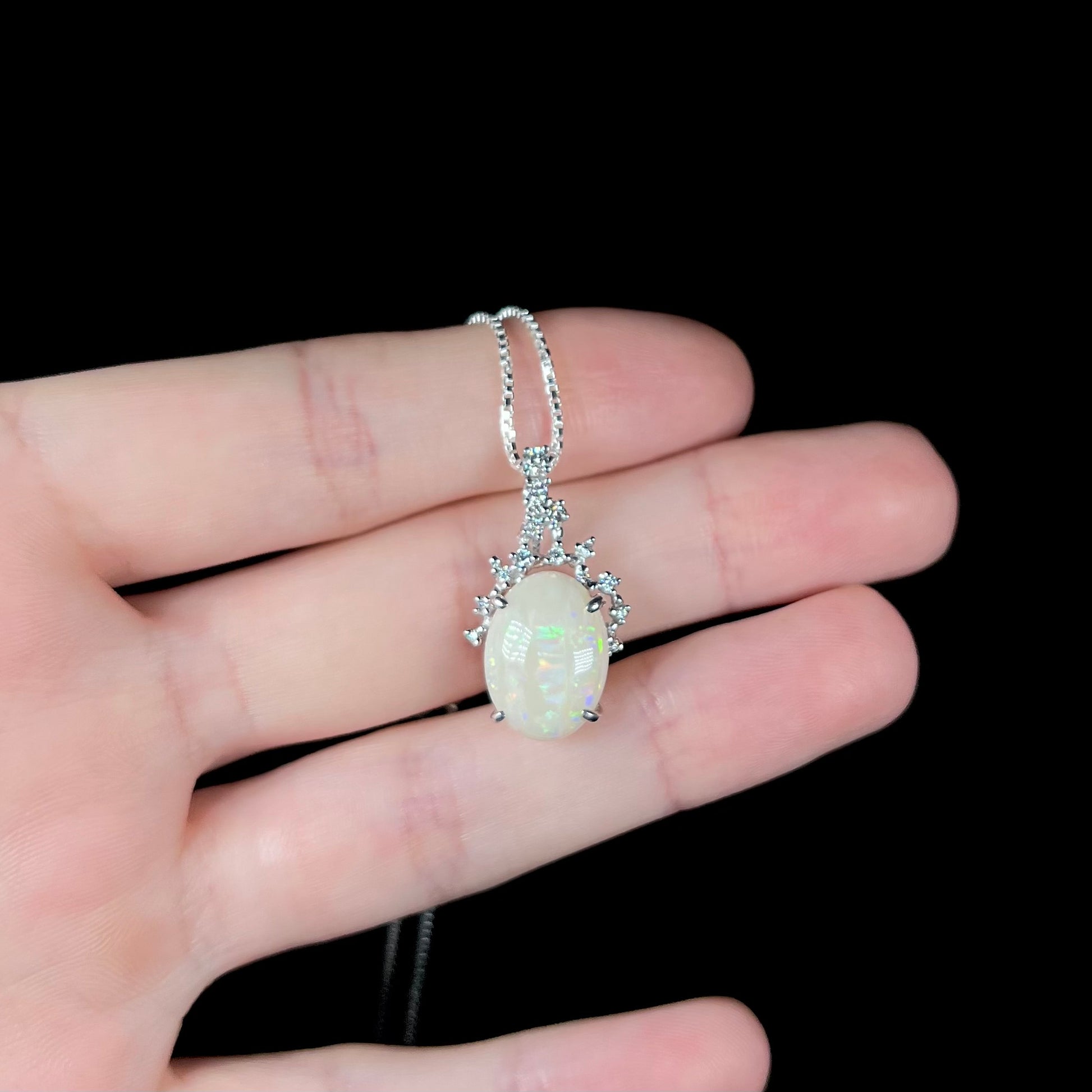 An opal and diamond necklace resting on fingers against a black background.