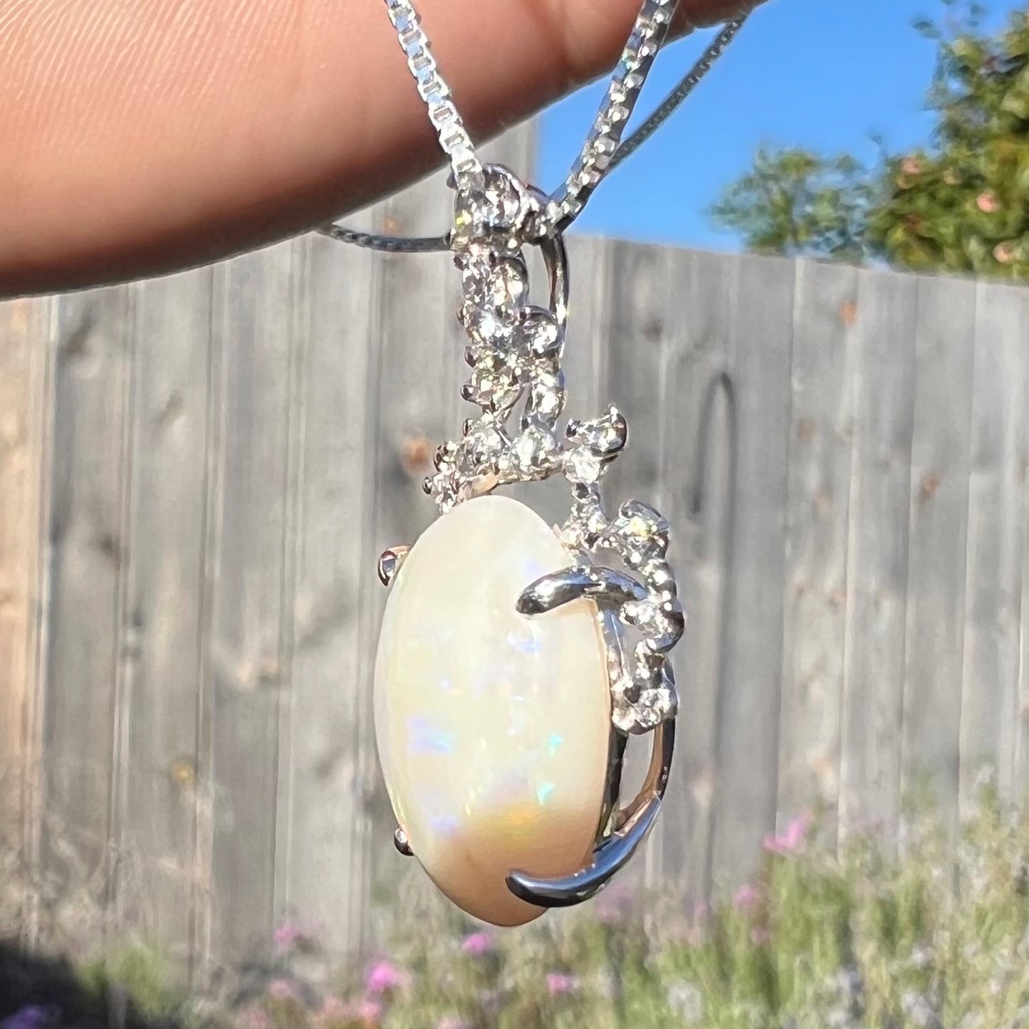 An opal and diamond necklace viewed from the opposite side in direct sunlight, where only a faint shimmer is present.