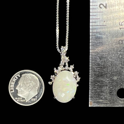 An opal and diamond necklace next to a dime and ruler for size comparison, measuring approximately one inch long.