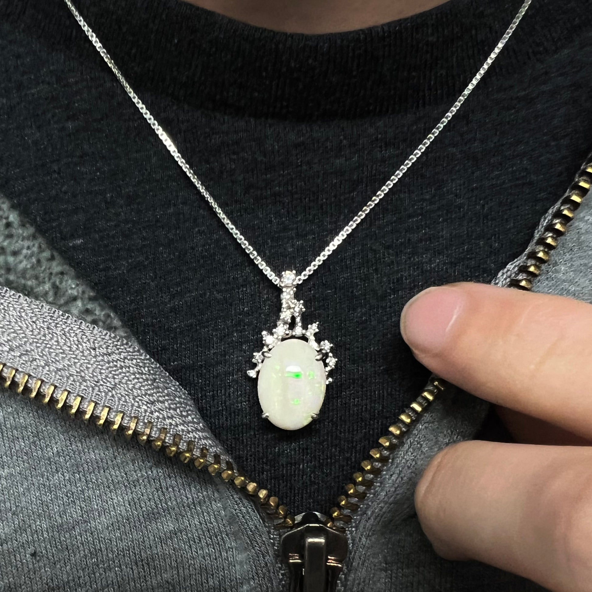 An opal and diamond necklace worn around the neck on a black T-shirt, showing a hint of green flash.