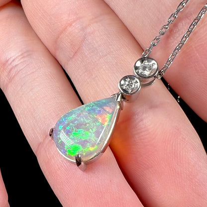 A platinum drop pendant mounted with two diamond accents and a pear shaped green-blue crystal opal.