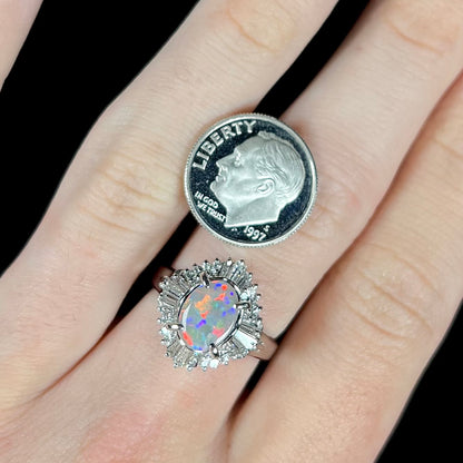 A semi-black opal and diamond spray-design ring in platinum, worn on a hand next to a US dime coin for scale.