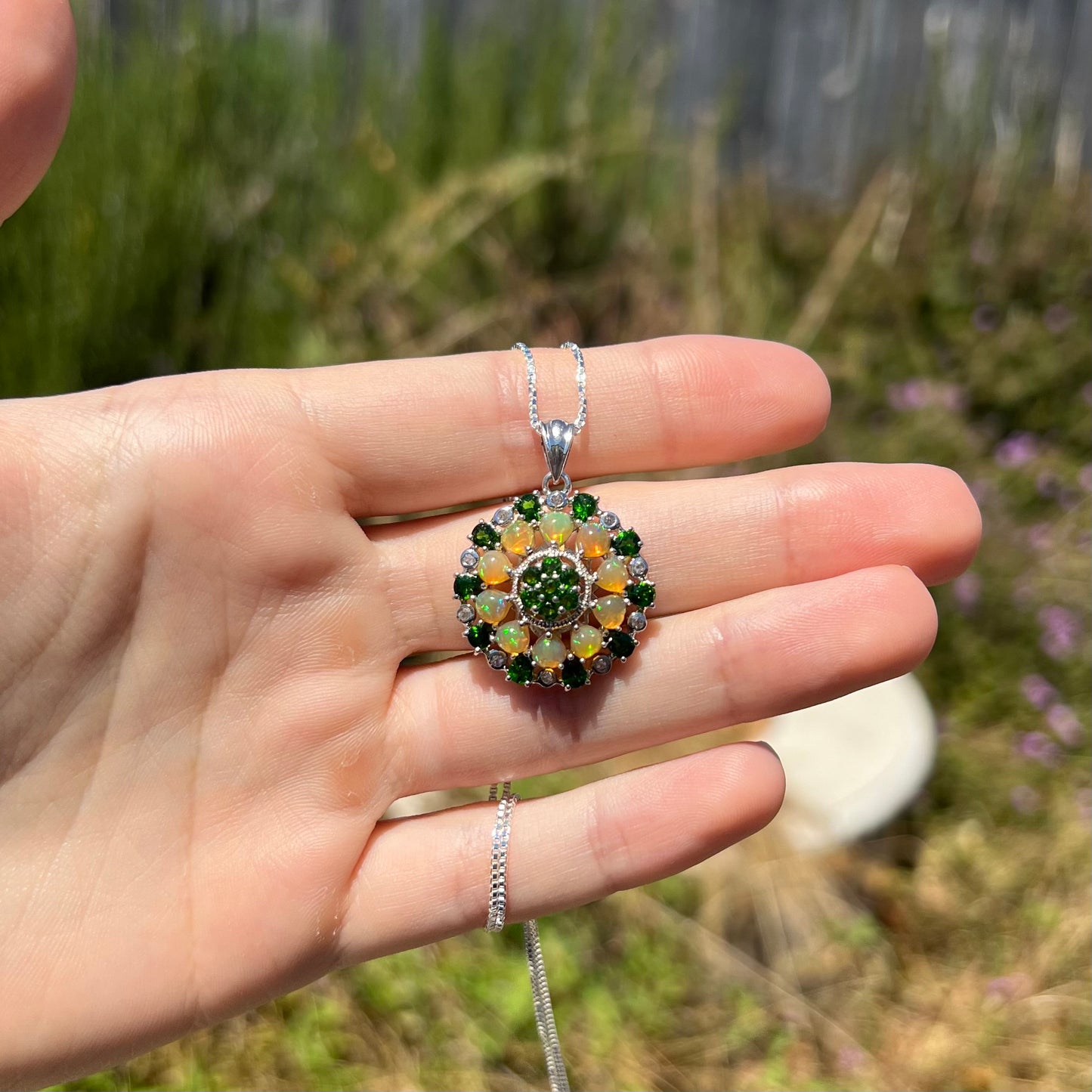 An opal and chrome diopside necklace, held in a hand at a distance in sunlight.