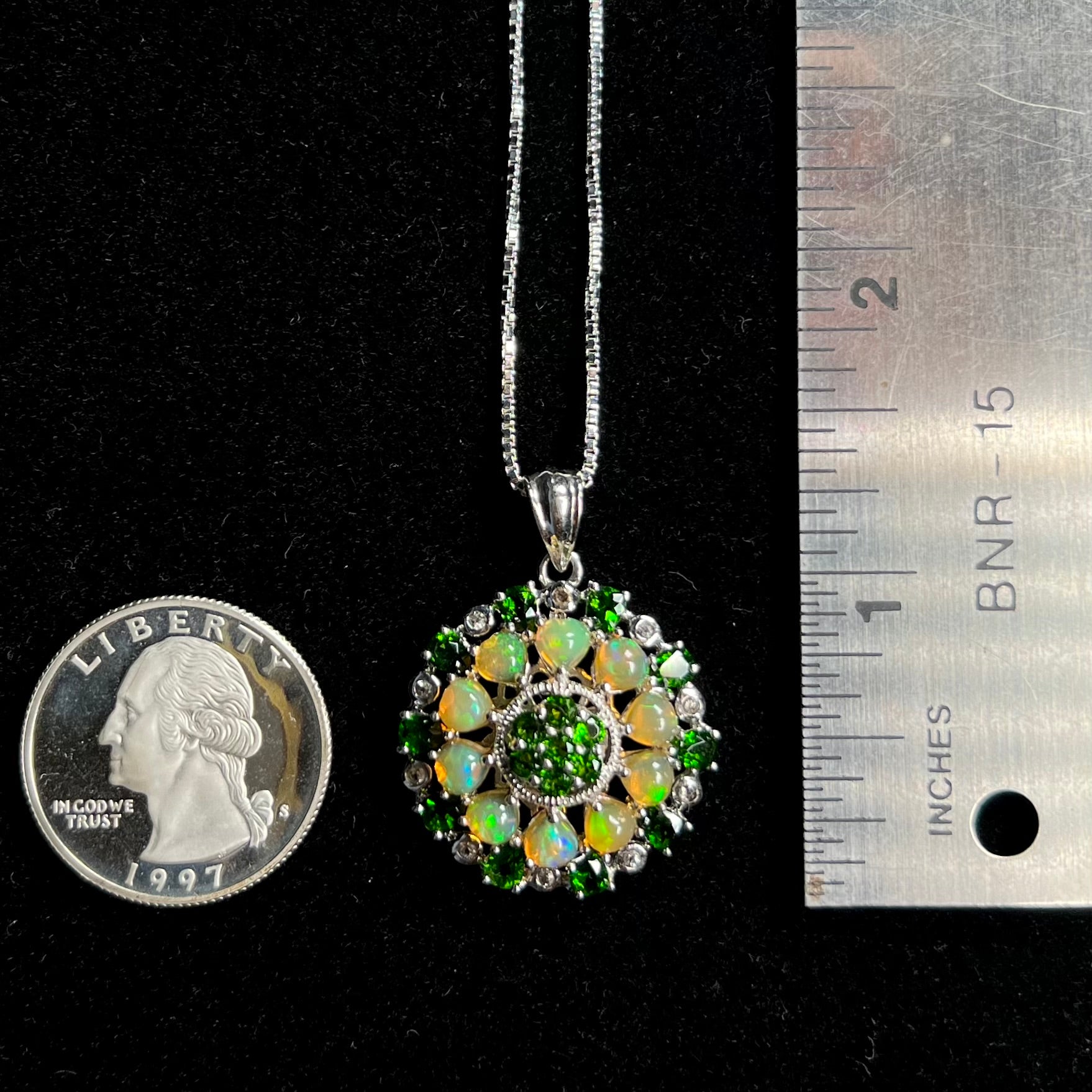 A silver Ethiopian opal and chrome diopside pendant that measures 1.33 inches long next to a quarter and ruler.