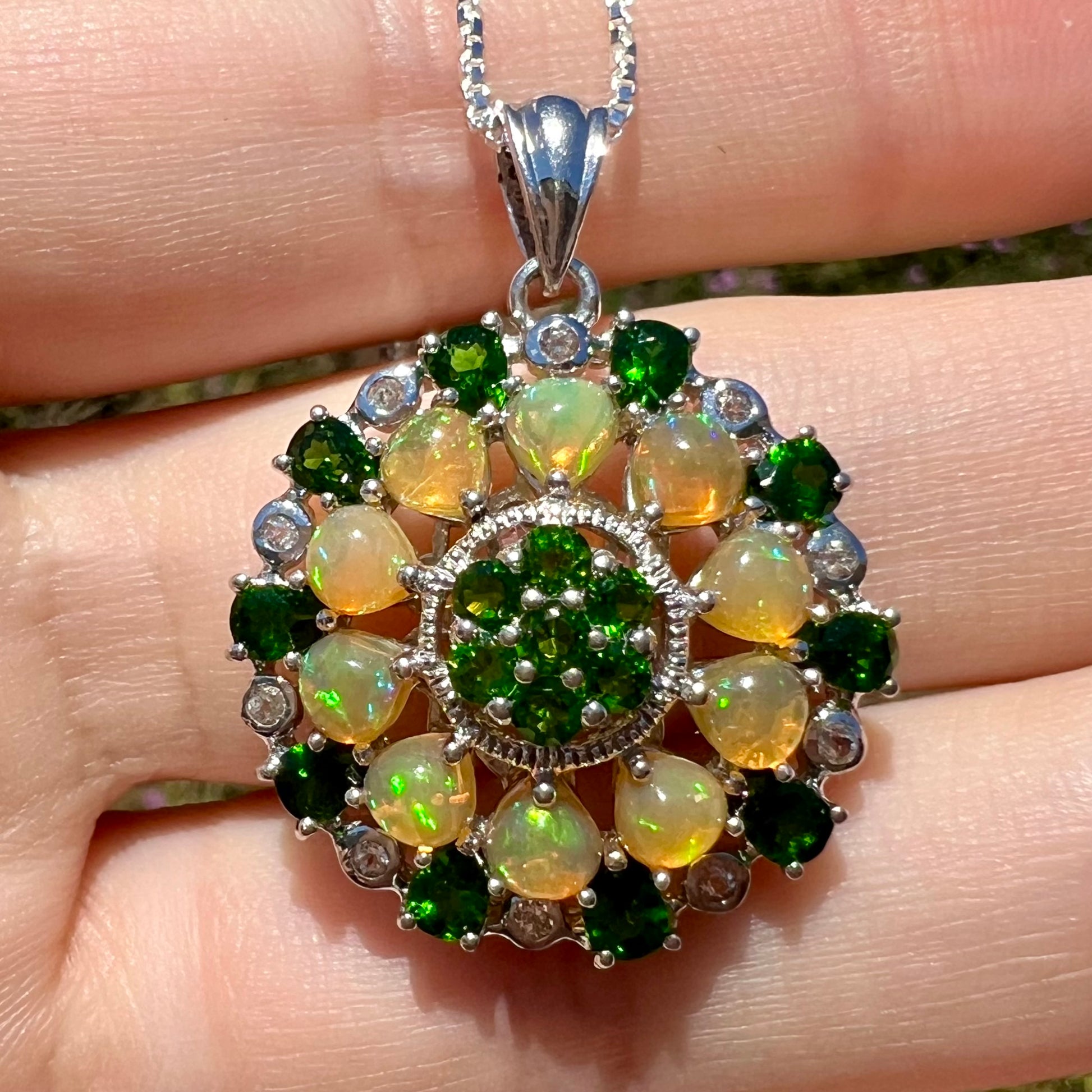 Close-up sunlit front view of an opal and chrome diopside pendant in sterling silver.