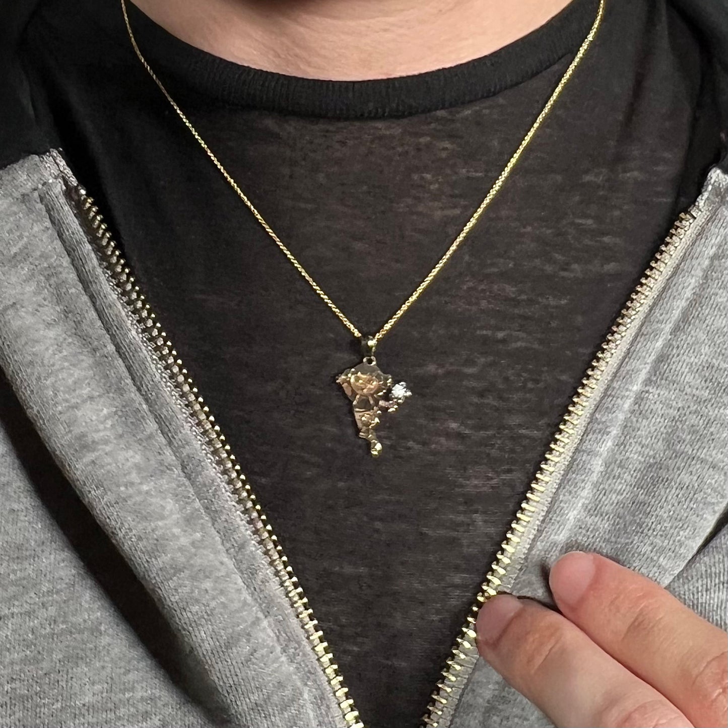 Person wearing gold-tone sterling silver Dora the Explorer opal necklace around neck under hoodie against dark shirt.