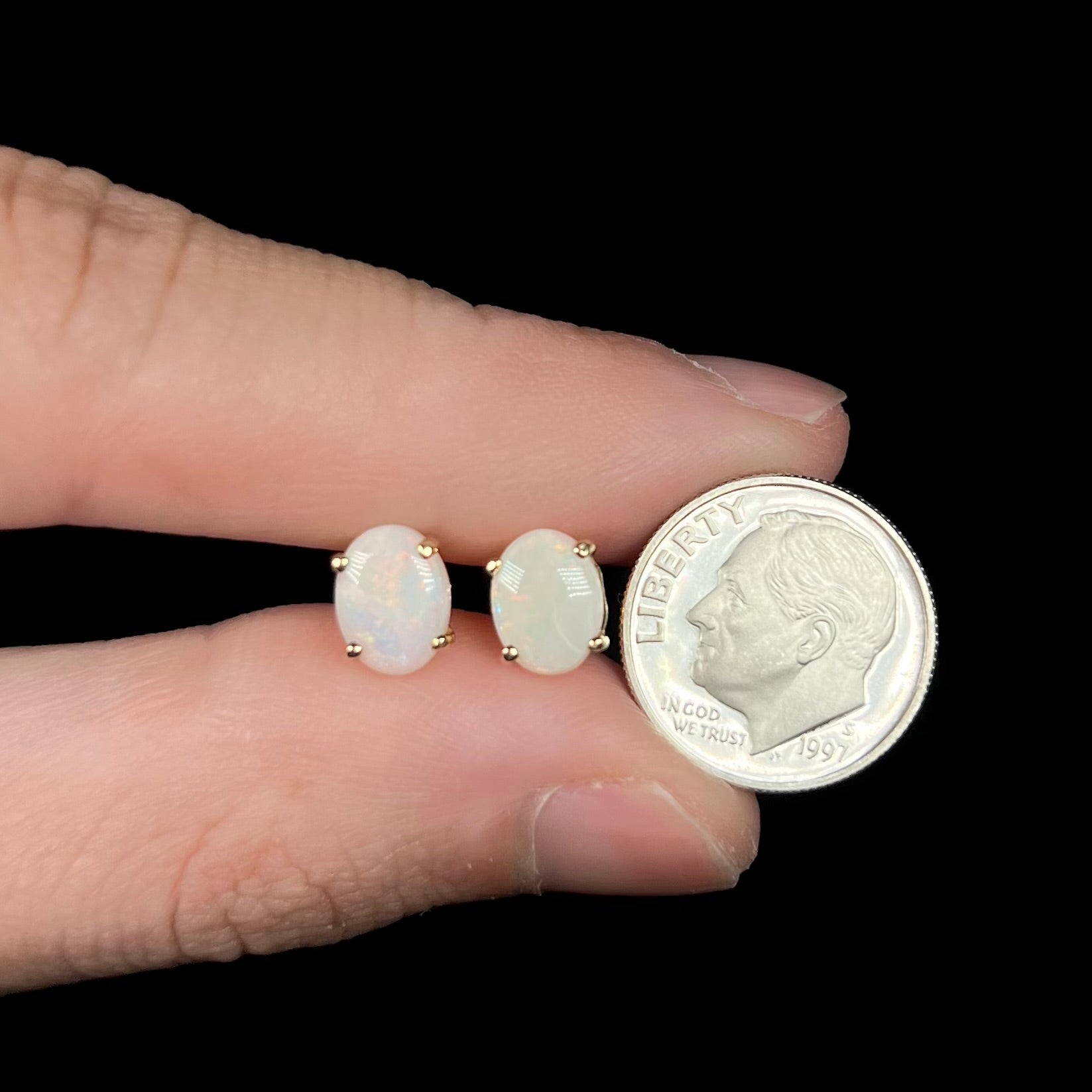 Opal earrings in fingers next to dime for size scale