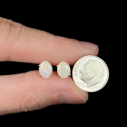 Opal earrings in fingers next to dime for size scale