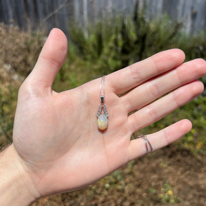 Hand holding natural Ethiopian opal and emerald cut cubic zirconia necklace in sunlight