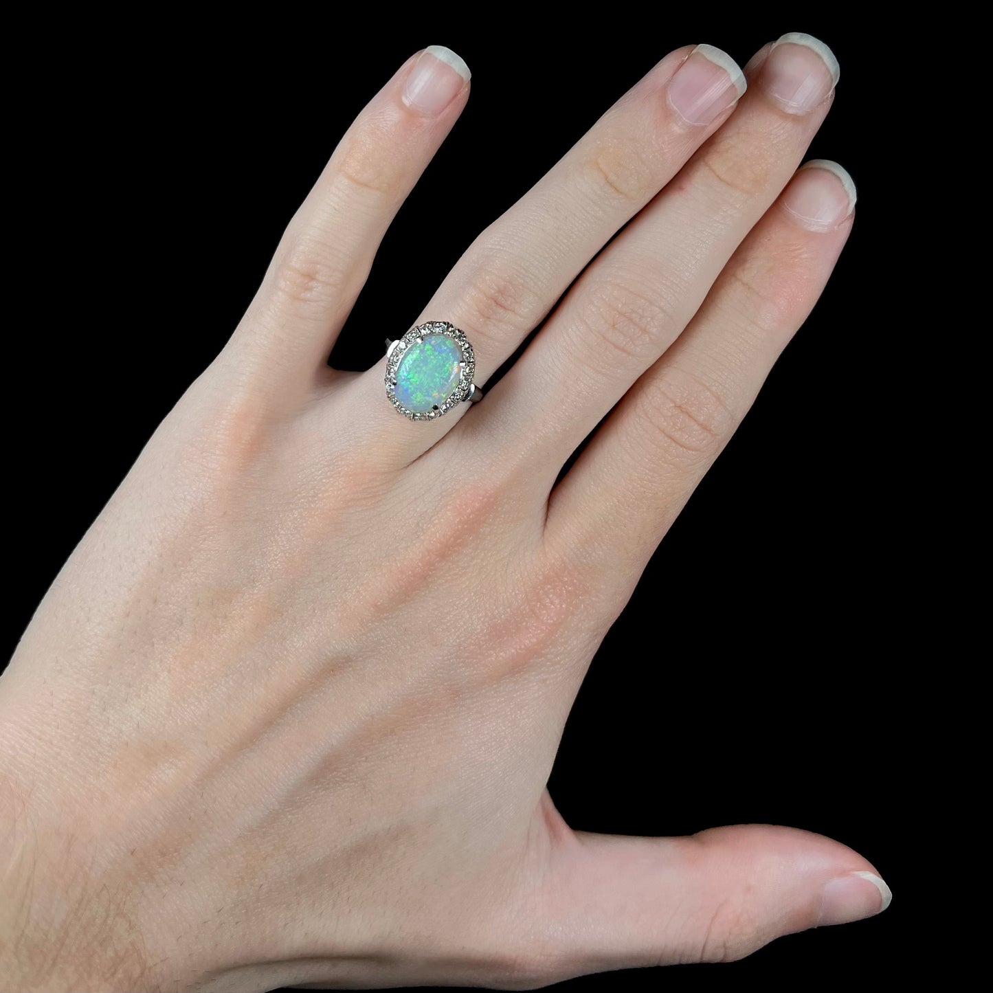 A vintage opal and diamond halo enagement ring on a hand.  The opal is green.