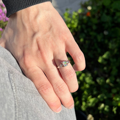 A platinum jelly opal engagement ring worn on a hand in natural sunlight.