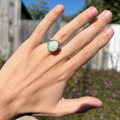 A large platinum opal engagement ring with diamond accents worn on a hand in sunlight.