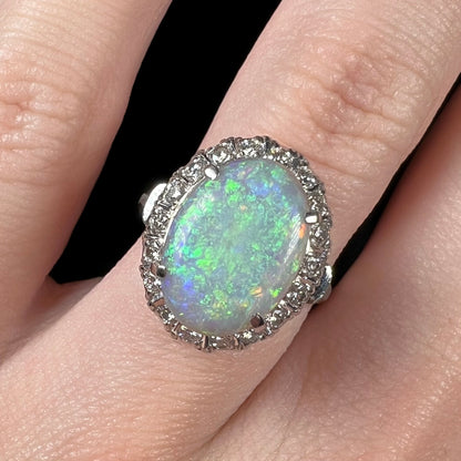 A vintage opal and diamond halo enagement ring on a finger.  The opal is green with blue overtones.