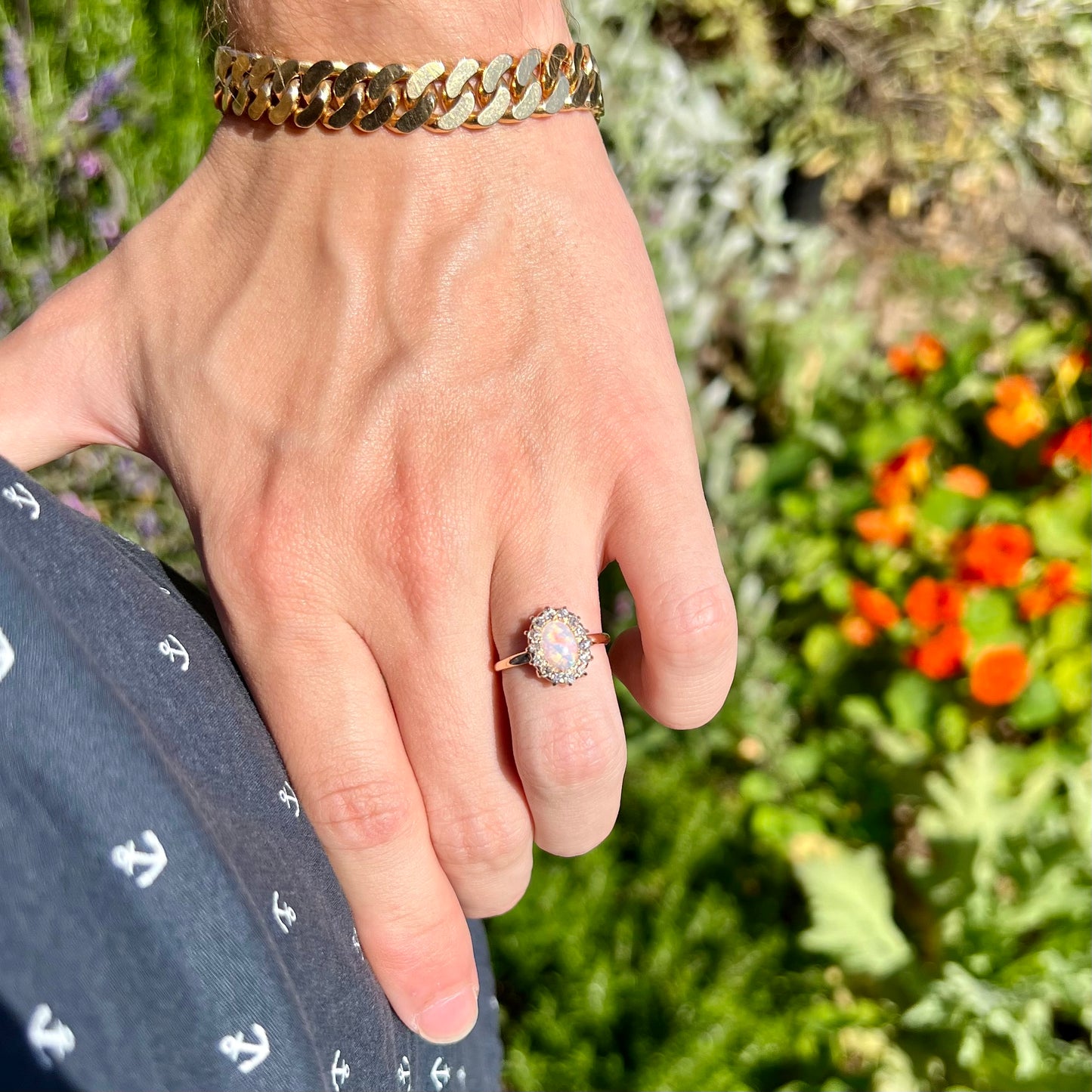 A yellow gold opal engagement ring being modeled in the sunlight on a hand.  The opal is set in a halo of diamonds.