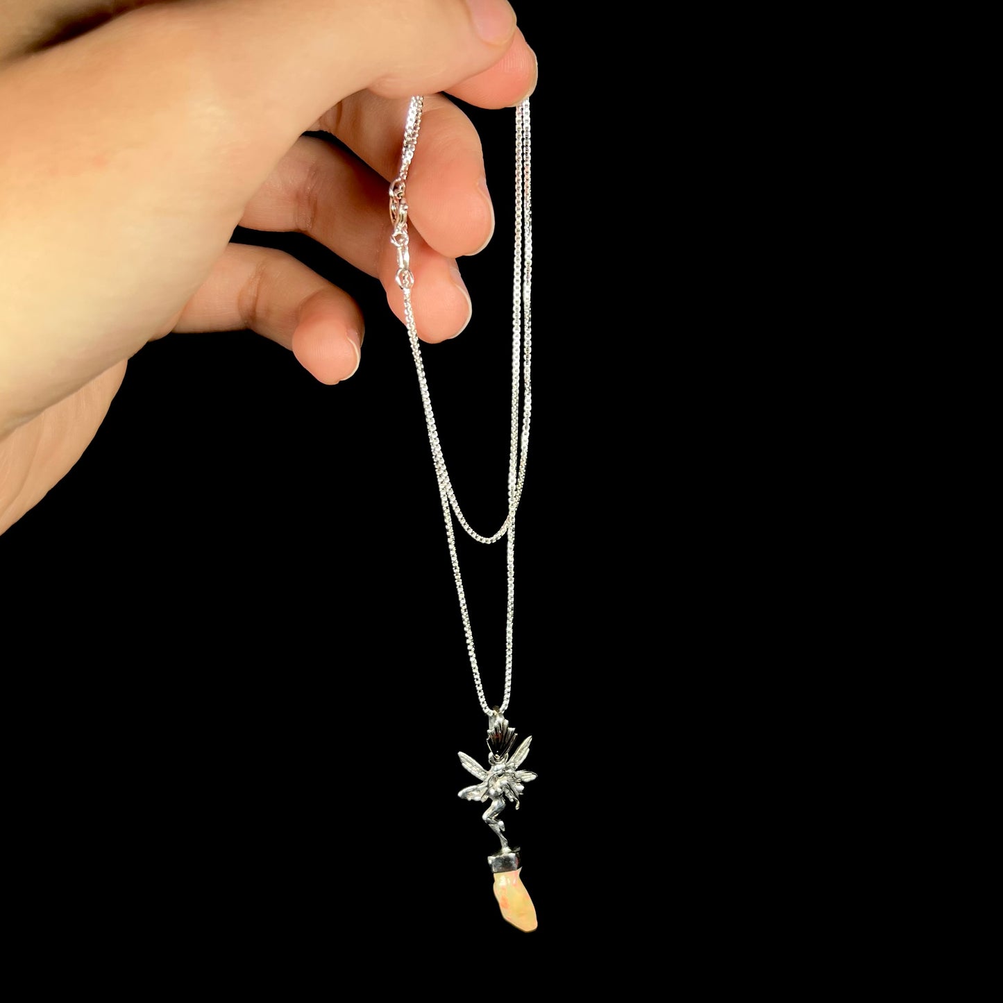 A sterling silver fairy necklace with an Ethiopian fire opal crystal, dangled from a hand by its chain.