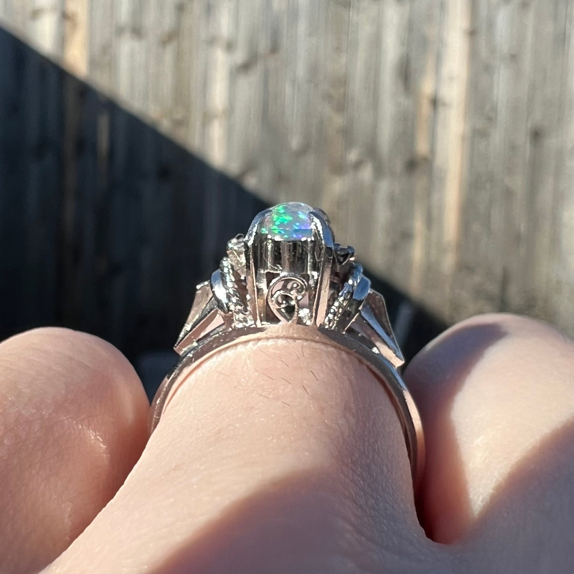 A dainty platinum opal filigree ring with diamonds worn on a finger in natural sunlight.