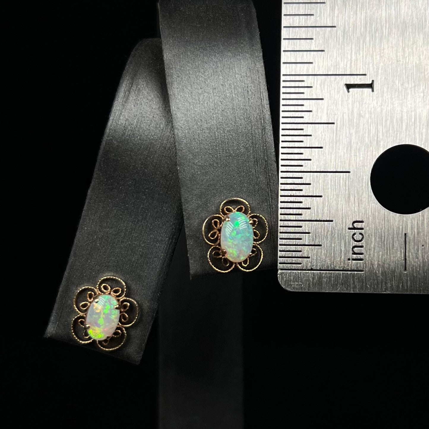Dainty pair of gold opal flower earrings next to a ruler for scale measuring 0.4 inches long