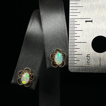 Dainty pair of gold opal flower earrings next to a ruler for scale measuring 0.4 inches long
