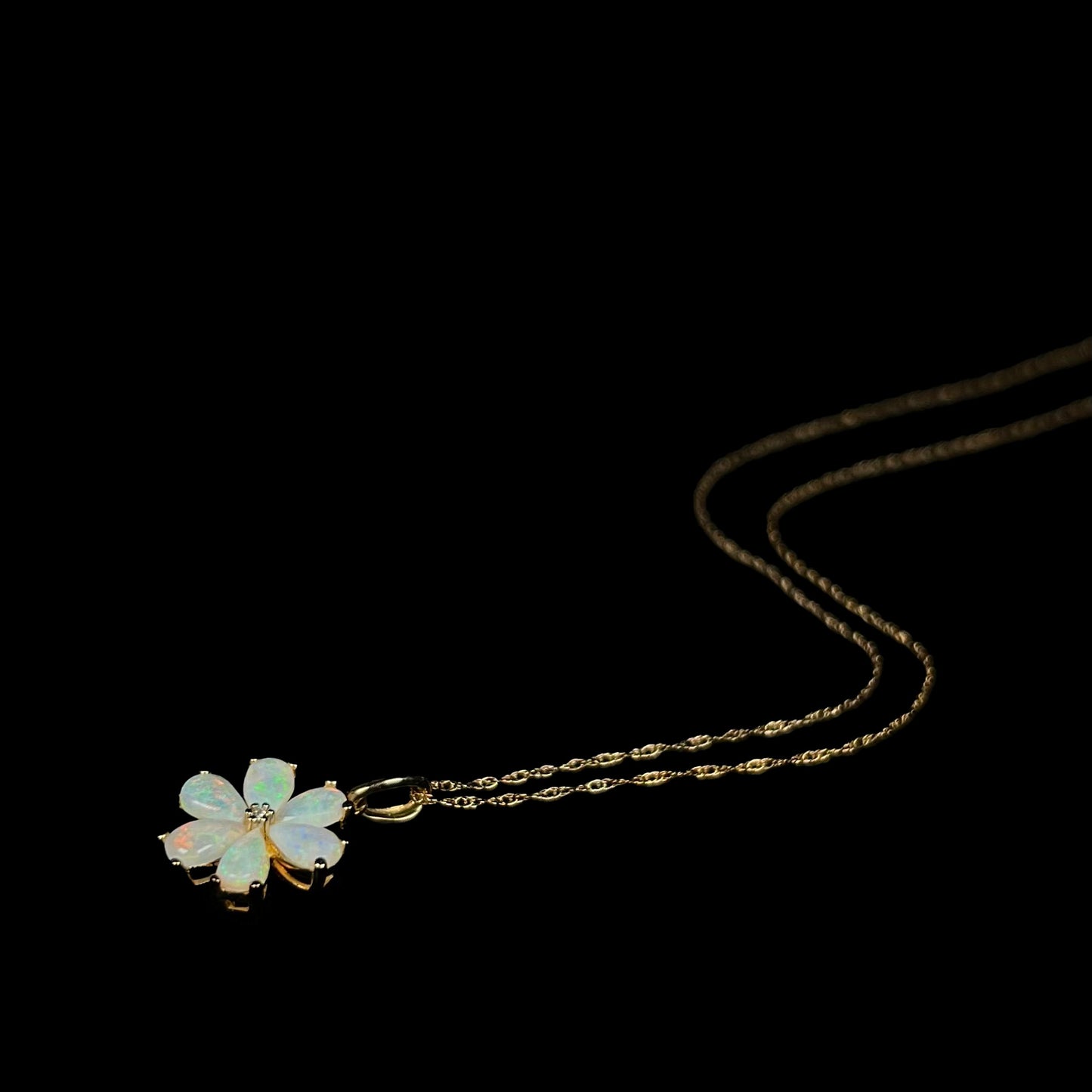 Gold Australian opal and diamond flower necklace shown laying on black backdrop