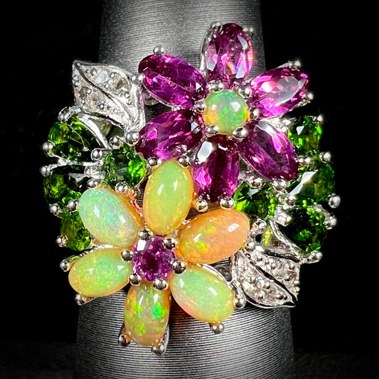 A sterling silver opal flower ring with garnet and chrome diopside accents, shown from the front.