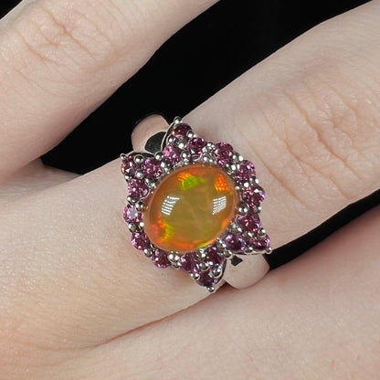 Close-up of women's fire opal ring with blowtie halo design set with purple rhodolite garnets, worn on finger