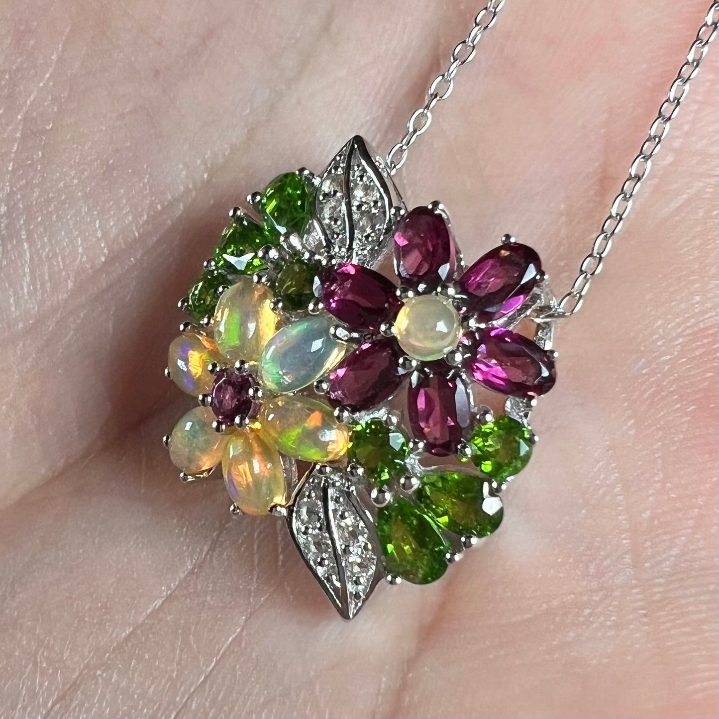 A sterling silver opal and garnet flower necklace shown close-up in the palm of a hand at an angle.