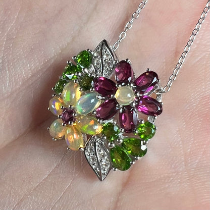 A sterling silver opal and garnet flower necklace shown close-up in the palm of a hand at an angle.