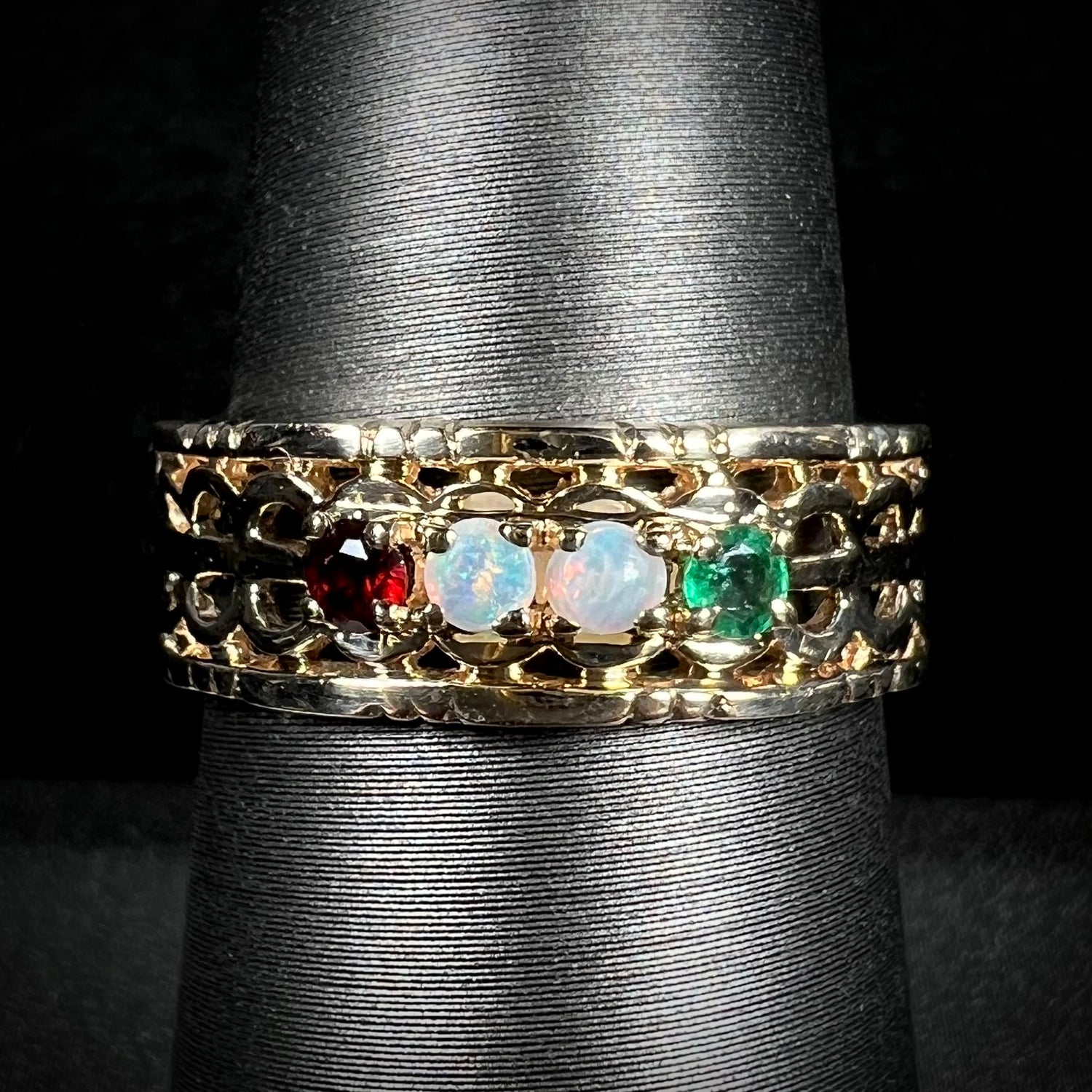 A gold woven-style mother's ring set with two opals, an emerald, and a garnet shown from the front.